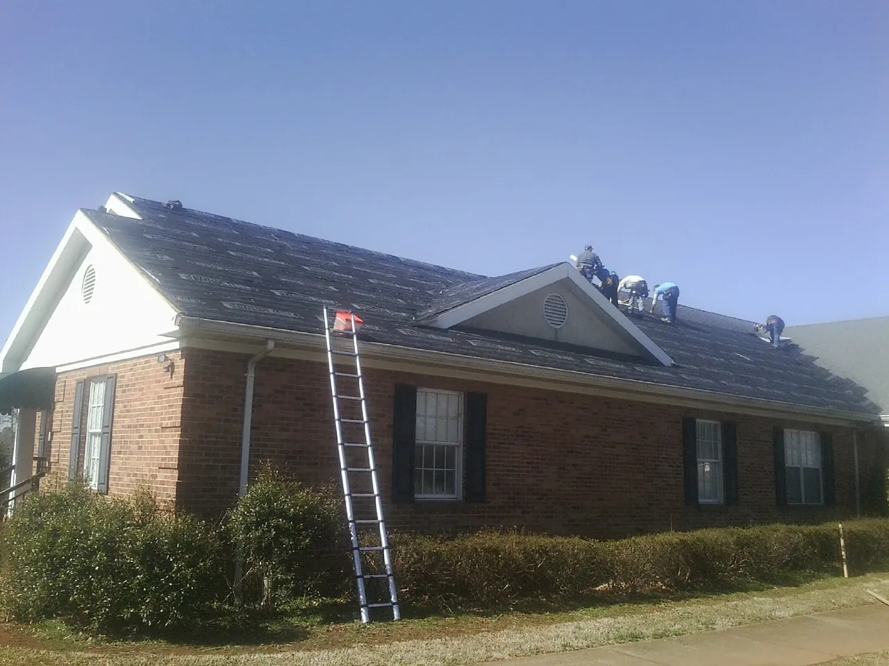 Crew tearing shingles off a brick ranch roof with a ladder set — Emergency Roof Repair work by our crew in Etta