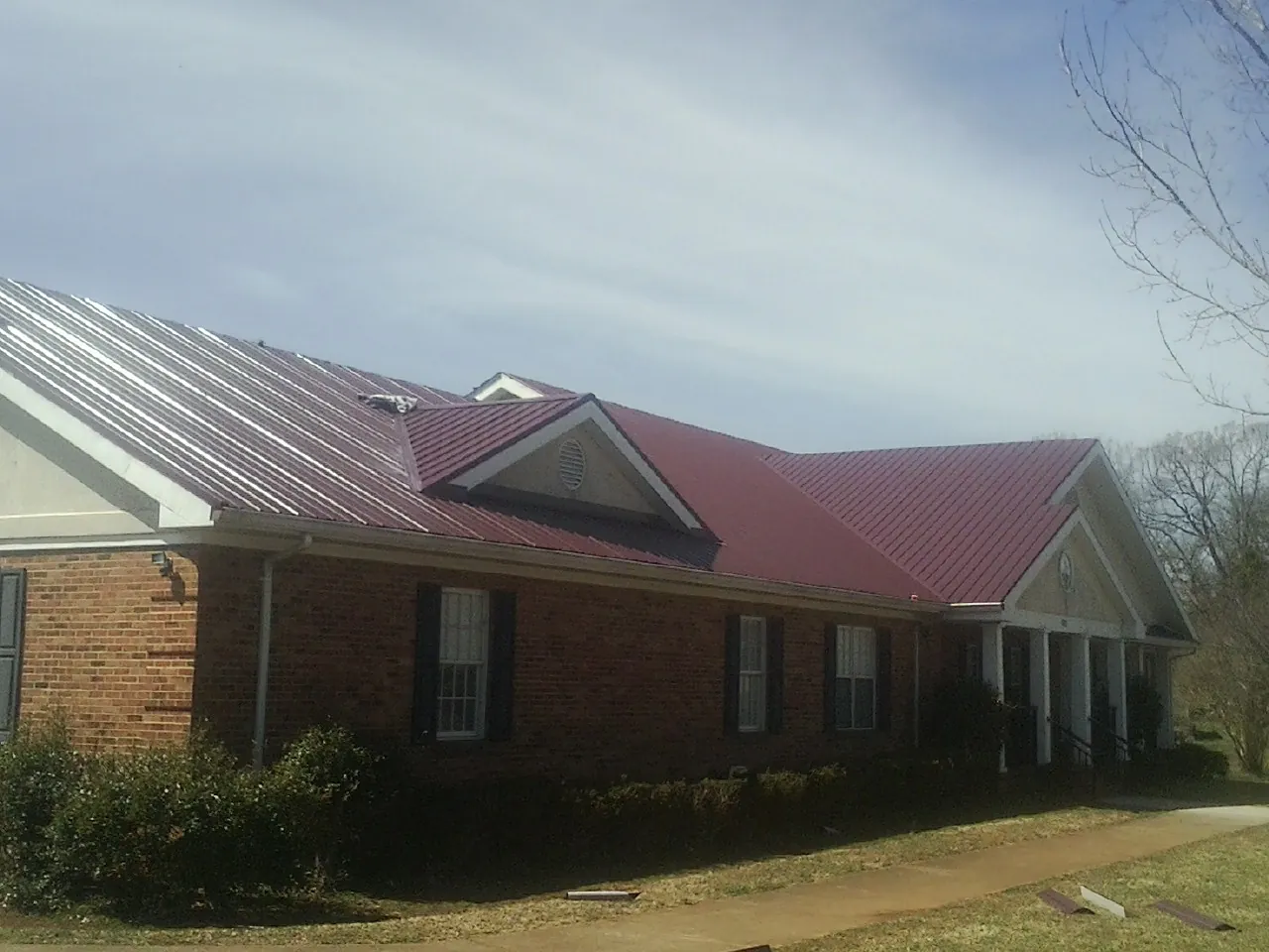Red metal roof with gabled entries on a long brick building, from a Hail Damage Roof Repair job in Etta