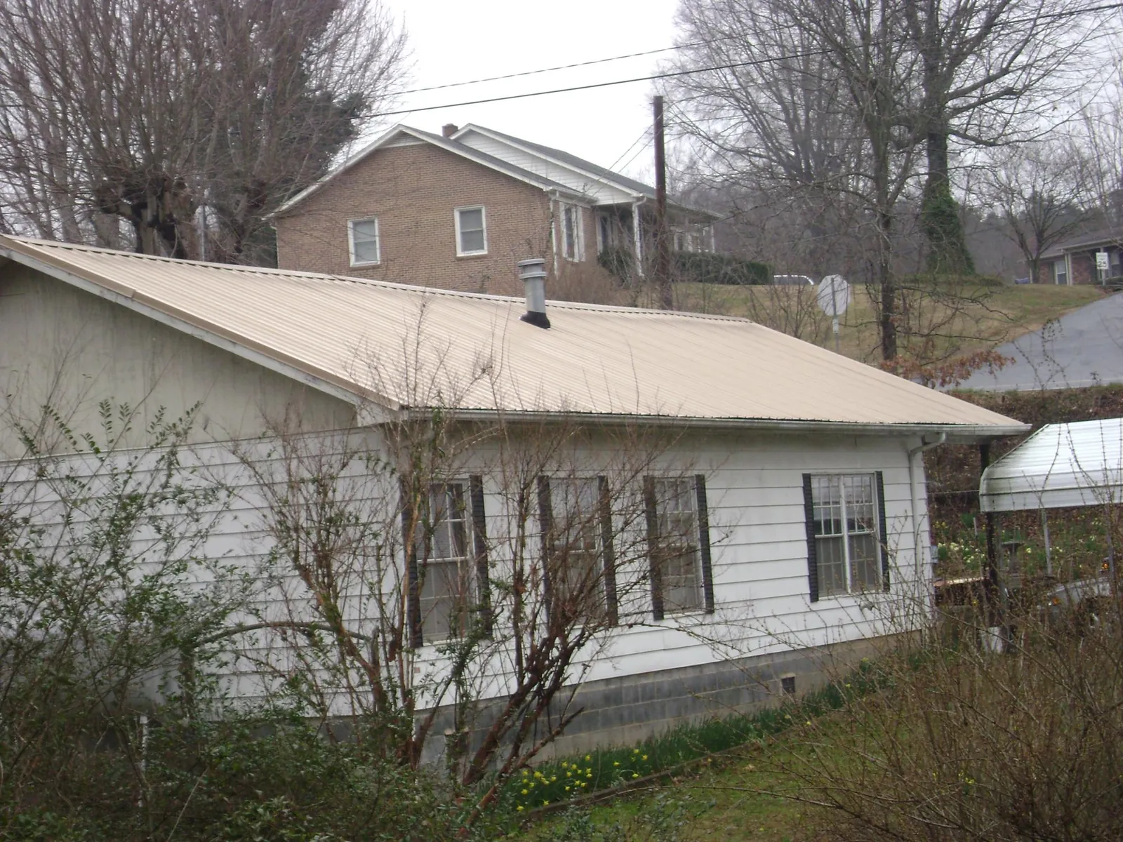 Tan metal roof on a white sided house set into a hillside — Commercial Roofing by Roofing Brothers in Etta